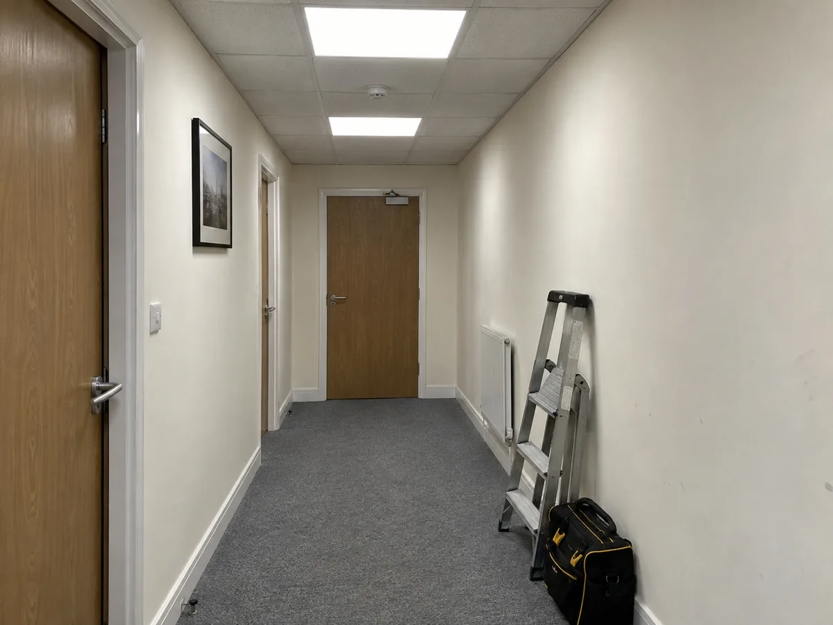 Illustrative photograph of an office corridor with lit LED panels, a folded ladder and a tool bag